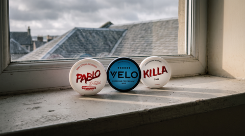 Three nicotine pouch cans of different brands on a grey concrete windowsill