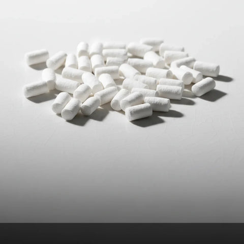 White cylindrical nicotine pouches scattered on a light grey surface with shadows beneath