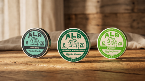 Three ALP nicotine pouch cans side by side on a warm oak surface, showing the 6mg and 12mg range