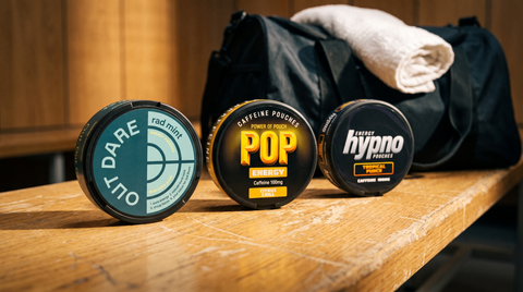 Three caffeine energy pouch cans lined up on a worn wooden gym locker-room bench