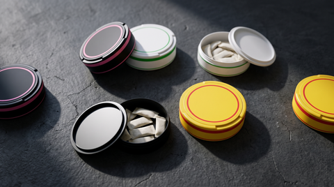 Several nicotine pouch cans open and closed scattered on dark concrete, photographed from above