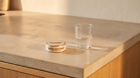 An OutDare CBD pouch can and a plain water glass on a pale concrete worktop