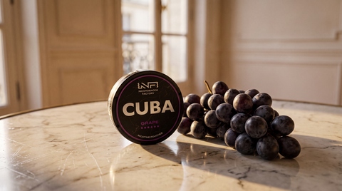 CUBA Black Grape nicotine pouch can on a pale marble bistro table with loose dark grapes nearby