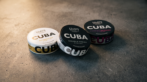 Three CUBA nicotine pouch cans in White and Black varieties clustered on a dark concrete surface