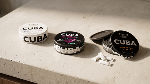 Three CUBA nicotine pouch cans of different product lines on a concrete worktop, one open