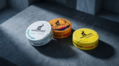 Three GREATEST nicotine pouch cans on dark concrete, showing ice, mango and lemonade varieties