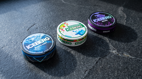 Three Iceberg Black nicotine pouch cans arranged in a loose arc on a dark granite worktop