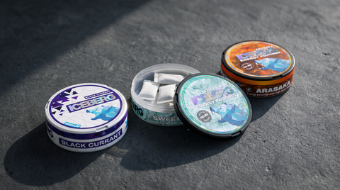 Row of ICEBERG nicotine pouch cans on dark concrete worktop, one open revealing white pouches