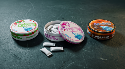 Three ICEBERG nicotine pouch cans on dark slate, one open revealing white pouches inside