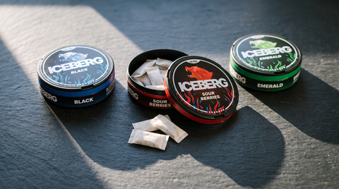 Three ICEBERG nicotine pouch cans on dark slate, the central one open showing white pouches