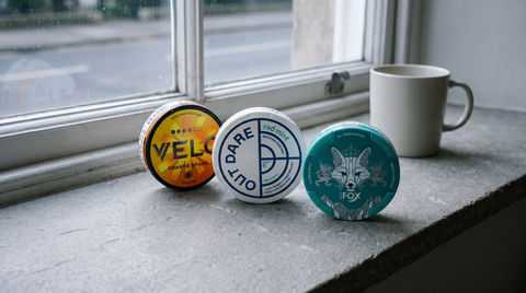 Three nic pouch cans standing on a grey stone windowsill in cool British daylight