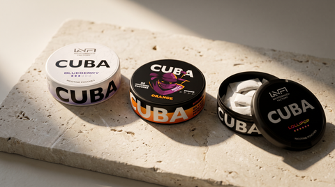 Three CUBA nicotine pouch cans — white, orange and black — arranged on a pale stone surface