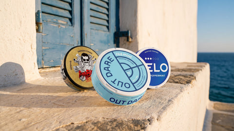OutDare, PABLO and VELO nicotine pouch cans on a whitewashed ledge on a Greek island