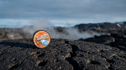 Nicotine pouch can on dark Icelandic basalt rock with pale geothermal steam rising behind