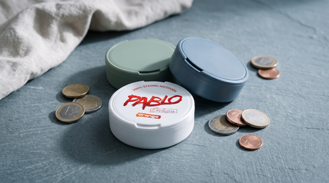 Several nicotine pouch cans clustered with euro coins on a cool grey slate surface