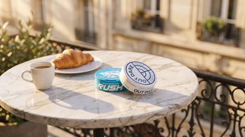 Two nicotine pouch cans on a marble bistro table in a warm Parisian courtyard setting