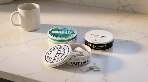 Three nicotine pouch cans loosely grouped on a white kitchen worktop beside a plain ceramic mug