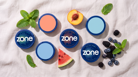 ZONE nicotine pouch cans photographed from above on linen, with fresh mint, peach and berries