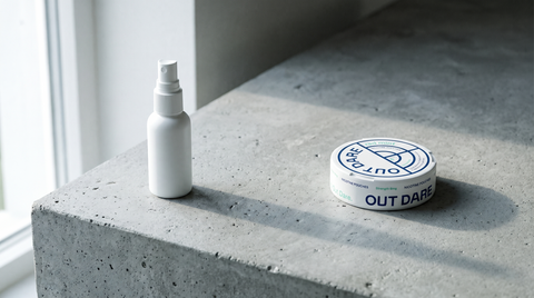 A plain nicotine spray bottle beside an OutDare nicotine pouch can on a concrete worktop