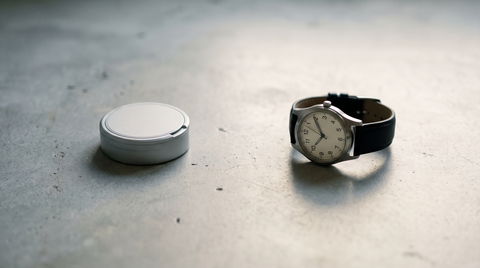 Analog wristwatch and a closed nicotine pouch can on a pale concrete worktop