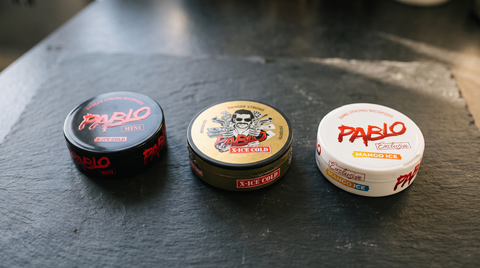 Three PABLO nicotine pouch cans standing in a row on a dark honed slate worktop