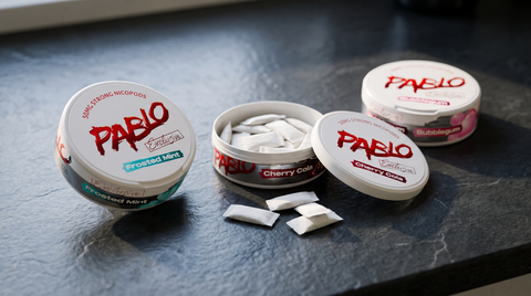 Three PABLO nicotine pouch cans on a dark slate surface, one open showing white pouches inside
