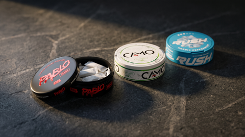 Three different nicotine pouch cans on a dark stone worktop, one open showing white pouches inside
