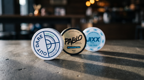 Three tobacco-free nicotine pouch cans lined up on a dark concrete café table