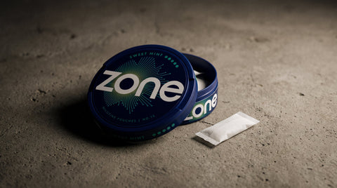 Zone branded blue tin and white pouch on textured grey concrete surface with dramatic studio lighting