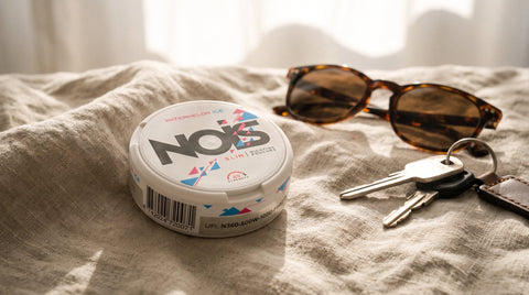 White circular NOX container on cream linen with tortoiseshell sunglasses and silver keys nearby