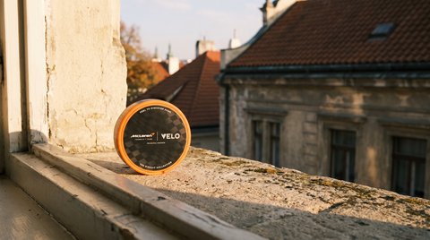 VELO McLaren Spicy Papaya nicotine pouch can on a stone ledge with blurred Central European rooftops behind