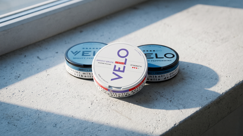Three VELO nicotine pouch cans in a staggered row on a pale concrete windowsill in cool daylight