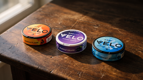 Three VELO nicotine pouch cans in a row on a dark oak surface
