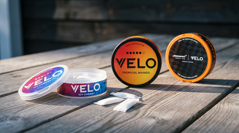 Three VELO nicotine pouch cans on a pine table in a warm lodge interior, one open