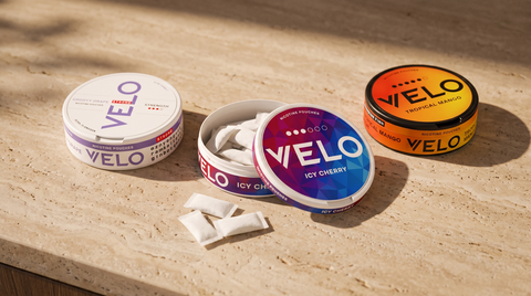 Three VELO nicotine pouch cans in different flavours arranged on a warm travertine surface