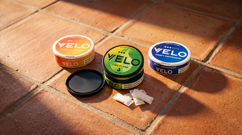 Three VELO nicotine pouch cans on terracotta tiles, one open showing white pouches inside