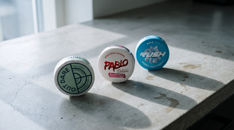 Three branded nicotine pouch cans on pale grey concrete in a W1NNAS nicotine pouches buyer's guide
