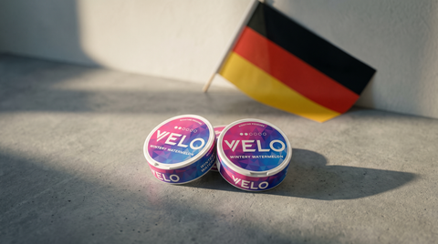 Round nicotine pouch cans on concrete beside a small black-red-gold German flag