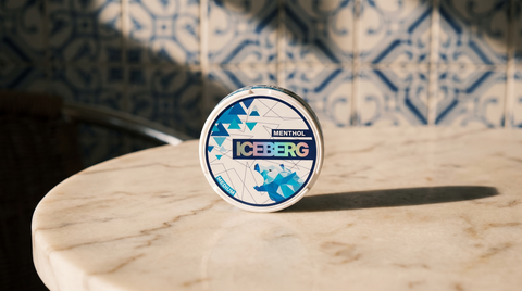 A nicotine pouch can on a marble café table with Portuguese blue-and-white azulejo tiles behind