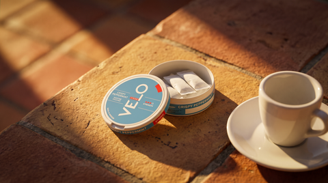 Open nicotine pouch can beside an espresso cup on sun-warmed terracotta tiles in Spain