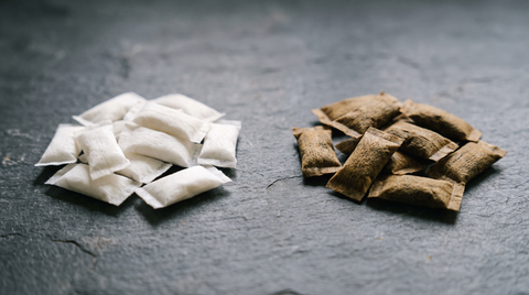 White nicotine pouches and brown tobacco pouches arranged side by side on a dark slate worktop