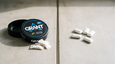 Open nicotine pouch can beside unwrapped chewing gum pieces on a concrete worktop